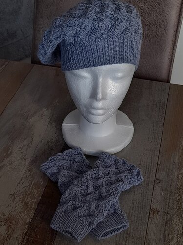 Gestrickte Slouch-Mütze und fingerlose Stulpen in hellblau-grau mit Zopfmuster auf einem Modellkopf