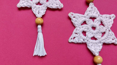 Detailed view of crochet star stitch pattern with wooden bead and white tassel on pink background
