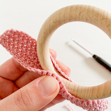 Hand hält Holzring mit rosa gehäkelten Ohren, Häkelnadel im Hintergrund