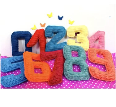 Assorted crocheted stuffed numbers 0 through 9 in bright colors on pink polka-dot fabric