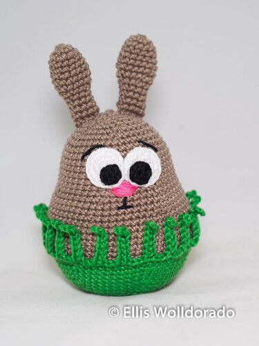 Detailansicht gehäkelter brauner Amigurumi-Hase mit applizierten Augen, rosa Nase und grünem Fransenrand