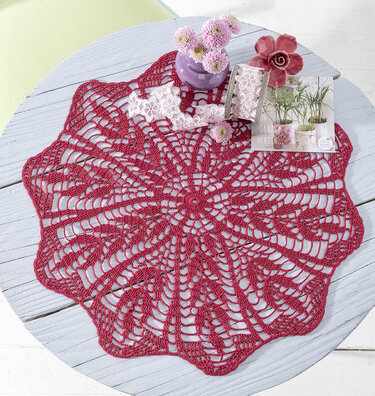 Rundes bordeauxfarbenes Häkeldeckchen mit floralem Spitzenmuster auf hellem Tisch