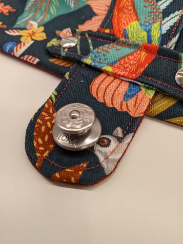 Nahaufnahme einer Kosmetiktasche mit tropischem Vogelprint, orangefarbenen Nähten und silbernem Druckknopf.