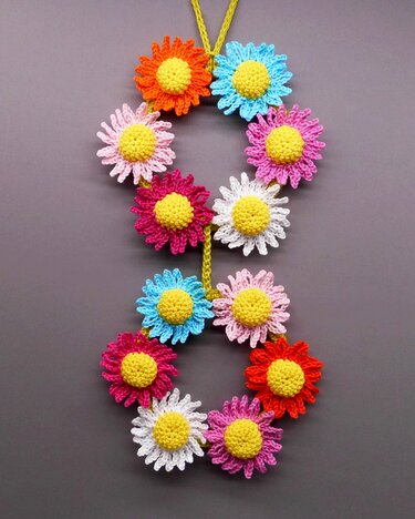 Crocheted garland of multicolored daisy flowers with yellow centers on a yellow cord against a gray background.