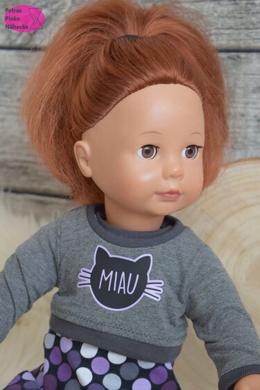 Puppe mit rotem Haar trägt graues Shirt mit schwarzem Katzenkopf und „MIAU“ Schriftzug