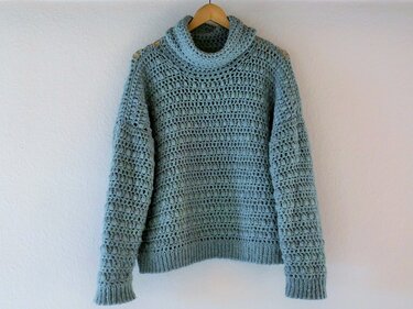 Hellblauer gehäkelter Damenpullover mit strukturierter Maschenarbeit und Rollkragen auf Holzbügel