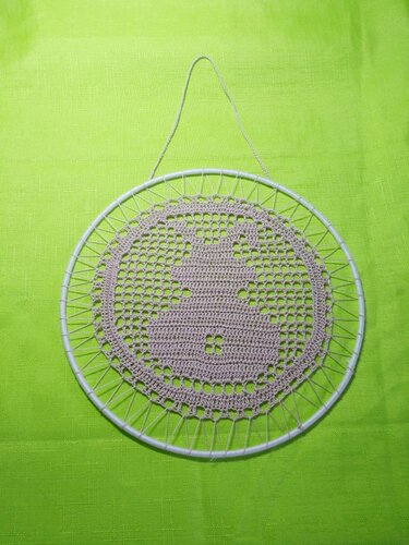 Beige gehäkelter Hase in weißem Ring, hängend vor grünem Stoff