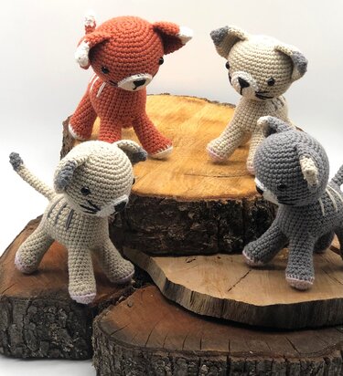 Vier gehäkelte Amigurumi-Katzen in Terrakotta, Beige und Grau auf Holzscheiben