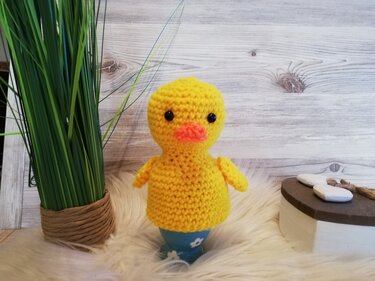 Gehäkelter gelber Küken-Eierwärmer mit orangem Schnabel auf blauem Eierbecher