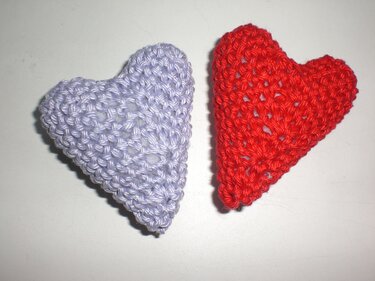 Zwei gehäkelte Herzen, rot und lavendelfarben, auf hellem Untergrund.
