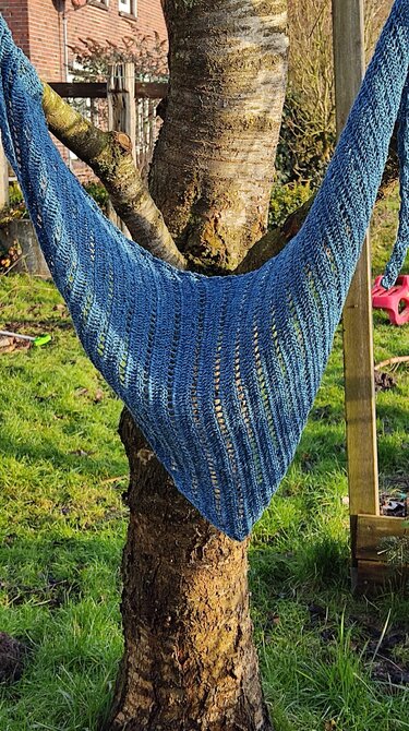 Blaues gehäkeltes Dreieckstuch mit vertikalen Lochreihen an einem Baum aufgehängt