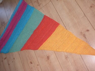 Gestricktes Dreieckstuch mit breiten Streifen (Magenta, Türkis, Mintgrün, Orange, Gelb) und feinem Glitzereffekt auf Holzboden.