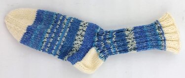 Handgestrickte Socke in Blau- und Cremetönen, liegend auf hellem Hintergrund