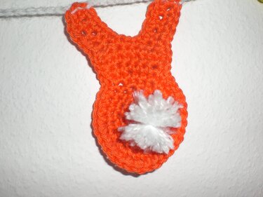 Nahaufnahme eines gehäkelten orangen Hasen mit flauschigem weißem Puschelschwanz an einer Schnur