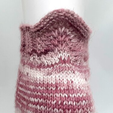 Nahaufnahme eines rosa-weiß gestreiften gestrickten Sockenbundes mit dekorativer Kante.