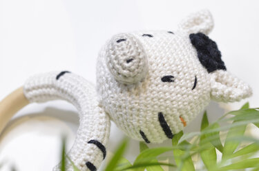 Gehäkelter weißer Greifring mit Tierkopf, schwarzen Details und hellem Holzring neben grünen Blättern.