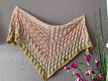 Gestricktes Dreieckstuch Rosé bis Gelb mit Lochmuster an grauer Wand