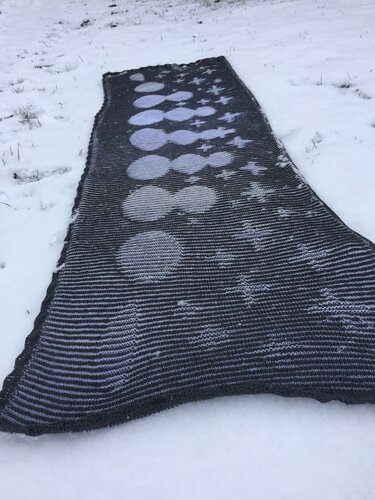 Dunkelgrauer gestrickter Schal mit hellgrauen Kreisen und Sternen auf Schnee.