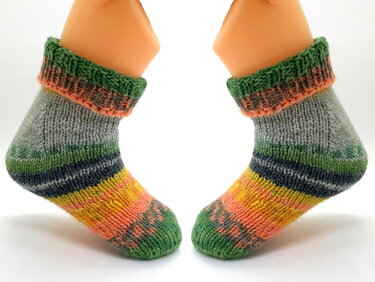 Gestrickte Babysocken mit bunten Ringelstreifen in Grün, Orange, Gelb und Grau auf Fußmodellen.