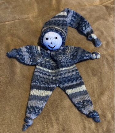 Gestrickter blaugrauer Stern-Greifling mit Gesicht und Zipfelmütze auf weichem Stoff.