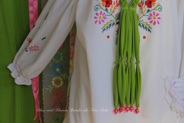 Weiße Bluse mit floraler Stickerei, gerüschten Ärmelbündchen und geknotetem grünem Zierband mit Perlen