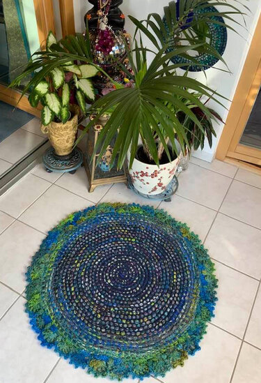 Runder gehäkelter Teppich auf weißen Fliesen neben Zimmerpflanzen und Spiegel