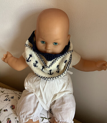 Puppe trägt gestricktes Halstuch mit dunkelblauen Ankern auf cremefarbenem Grund.