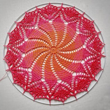 Rundes gehäkeltes Spitzen-Deckchen in Orange‑Pink mit Spiralmuster auf Blockring