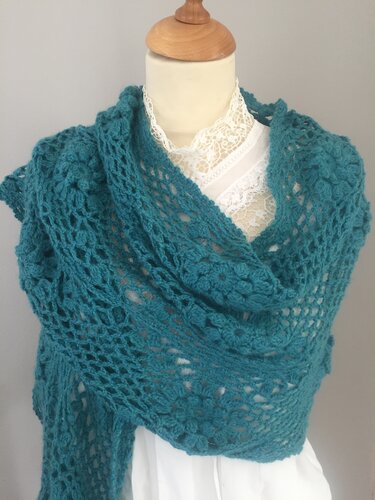 Teal crocheted shawl with lace-like openwork pattern draped on a mannequin over a white blouse.
