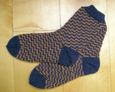 Gestrickte Herrensocken in Blau und Braun mit Zickzackmuster auf Holzuntergrund