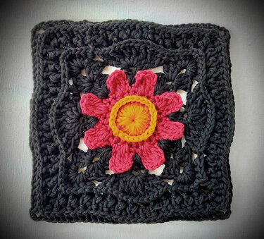 Gehäkeltes dunkles Quadrat mit rosa Blüte und gelbem Zentrum