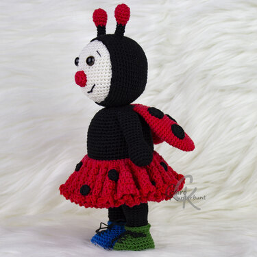 Gehäkeltes Marienkäfer-Amigurumi mit rotem Rock, schwarzen Punkten, Flügeln und bunten Schuhen auf weißem Hintergrund
