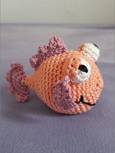 Gehäkelter Amigurumi-Fisch orange mit lila Flossen auf grauem Hintergrund