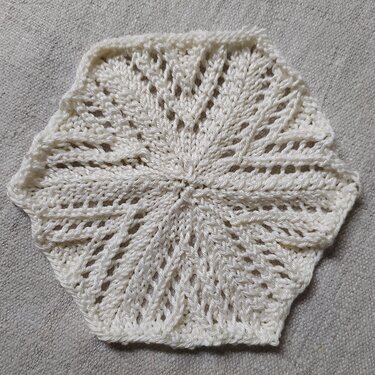 Weiße sechseckige Strickapplikation mit Ajourmuster auf hellem Untergrund