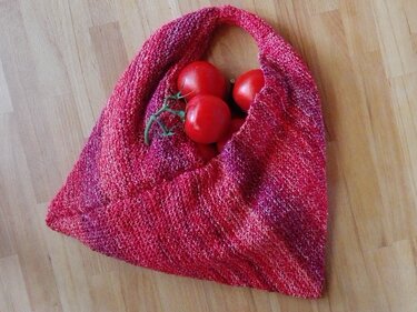 Handgestrickte mehrfarbige Einkaufstasche in Rot- und Rosatönen mit Tomaten auf Holzboden
