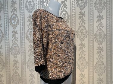 Seitliche Ansicht eines Damen-Strickpullovers in melierter Melange-Optik mit schwarzen Bündchen und 3/4-Ärmeln auf einer Schaufensterpuppe.