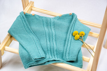 Türkiser gestrickter Baby-Pullover mit Schulterknöpfen auf Holzgestell