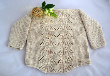 Gestrickter hellbeiger Babypullover mit zentralem Fächermuster und langen Ärmeln, auf hellem Hintergrund.