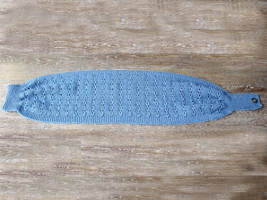 Hellblauer schmaler gestrickter Schal mit Ajourmuster und Knopf, flach auf Holzuntergrund gelegt