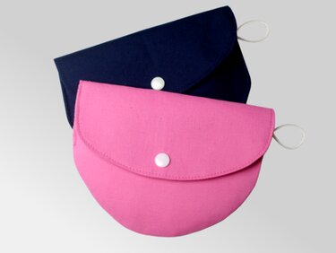 Pinkes und dunkelblaues Stofftäschchen mit gewölbter Klappe und weißem Knopf.