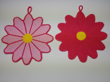 Zwei gestrickte Blumentopflappen in Rosa und Dunkelrosa mit gelber Mitte und Aufhängeschlaufe.