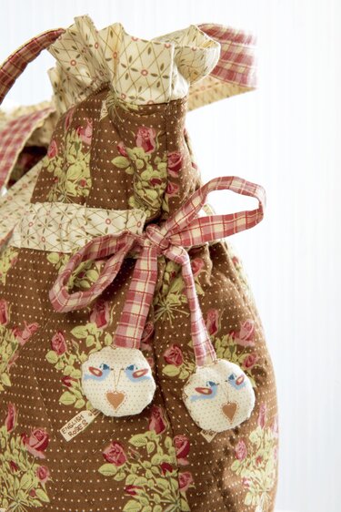 Brauner Stoffbeutel mit Blumenmuster, Kordelzug und runden Stoffanhängern