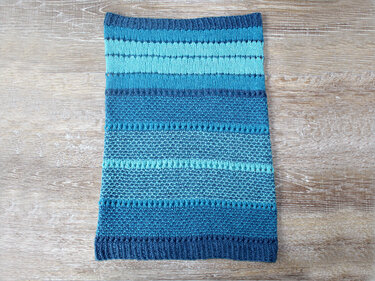 Gestrickter Loop mit Rippbündchen, kraus rechten und glatt rechten Bereichen sowie Lochreihen in Blau- und Türkistönen