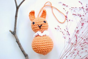 Gehäkelte orangefarbene Hasenrassel mit weißem Kragen und Aufhängeschlaufe