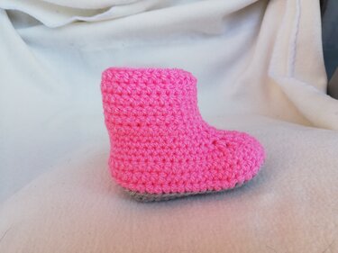 Rosafarbenes gehäkeltes Babystiefelchen mit grauer Sohle auf hellem Stoff