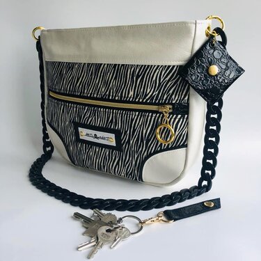 Schwarz-weiße Umhängetasche mit Zebra-Muster, schwarzem Kettenträger und goldfarbenen Details.