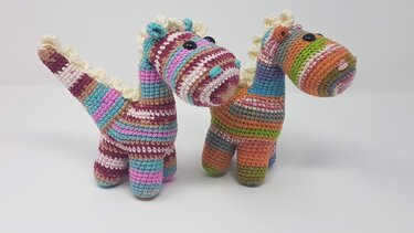 Zwei bunt gestreifte gehäkelte Amigurumi-Dinosaurier mit heller Rücken-Zackenreihe