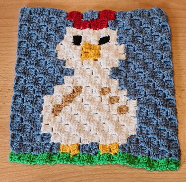 Kachelartiges Häkelquadrat mit Huhn in kontrastreichen Farbblöcken