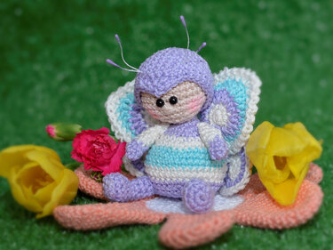 Gehäkelte pastellfarbene Schmetterlings-Amigurumi auf einer Häkelblume