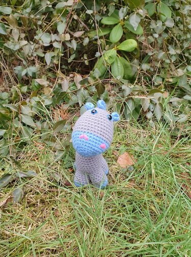Gehäkeltes Dino-Amigurumi grau mit hellblauem Maul und rosa Bäckchen im Gras